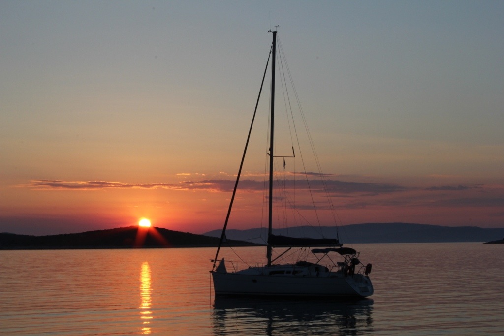 A sailboat silhouetted against a sunset over the sea