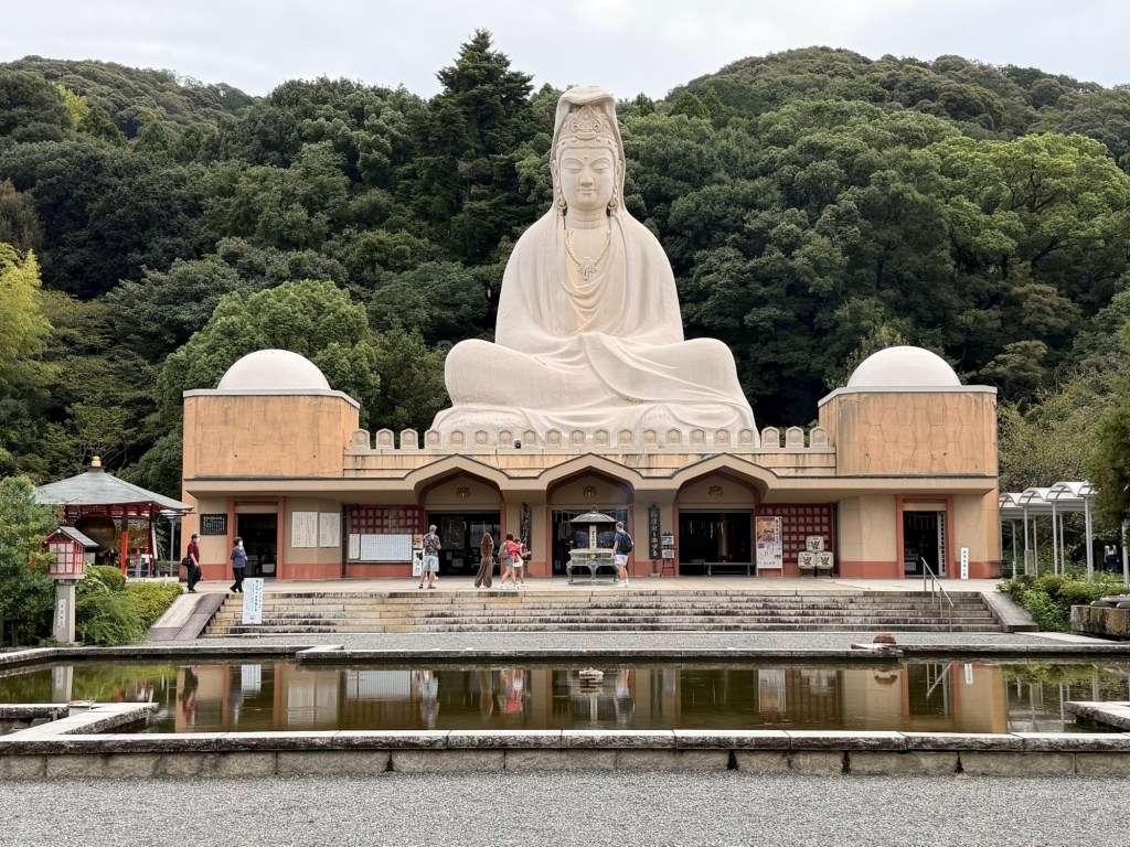 A giant white Kannon statue with a temple building in Japan.